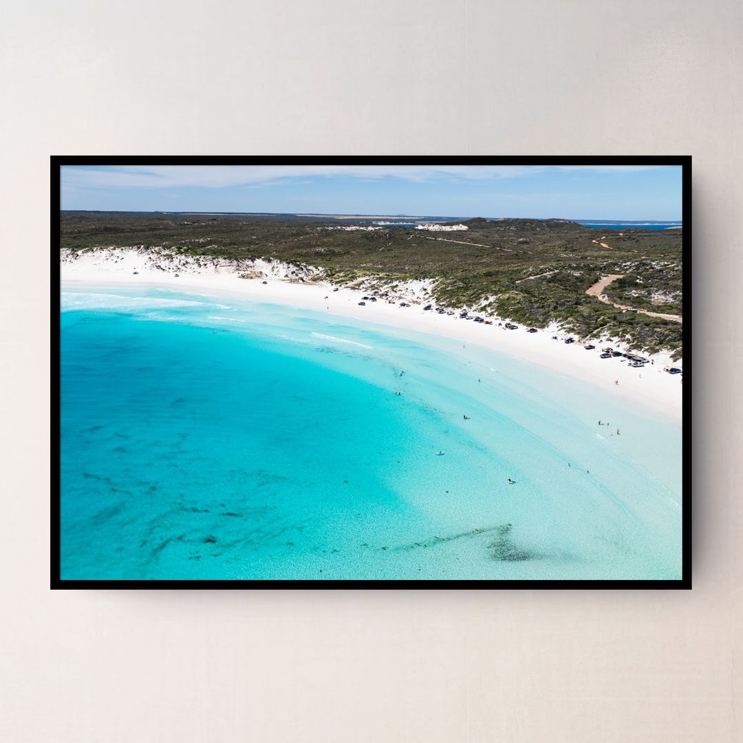 A black framed aerial photograph of Wharton  Beach Esperance Australia with turquoise water, white sand, and green vegetation, displayed on a light beige wall.