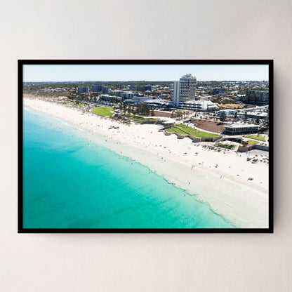 A black framed aerial photograph of a Scarborough Beach Perth WA with turquoise ocean water, white sand, and coastal buildings, displayed on a light beige wall.