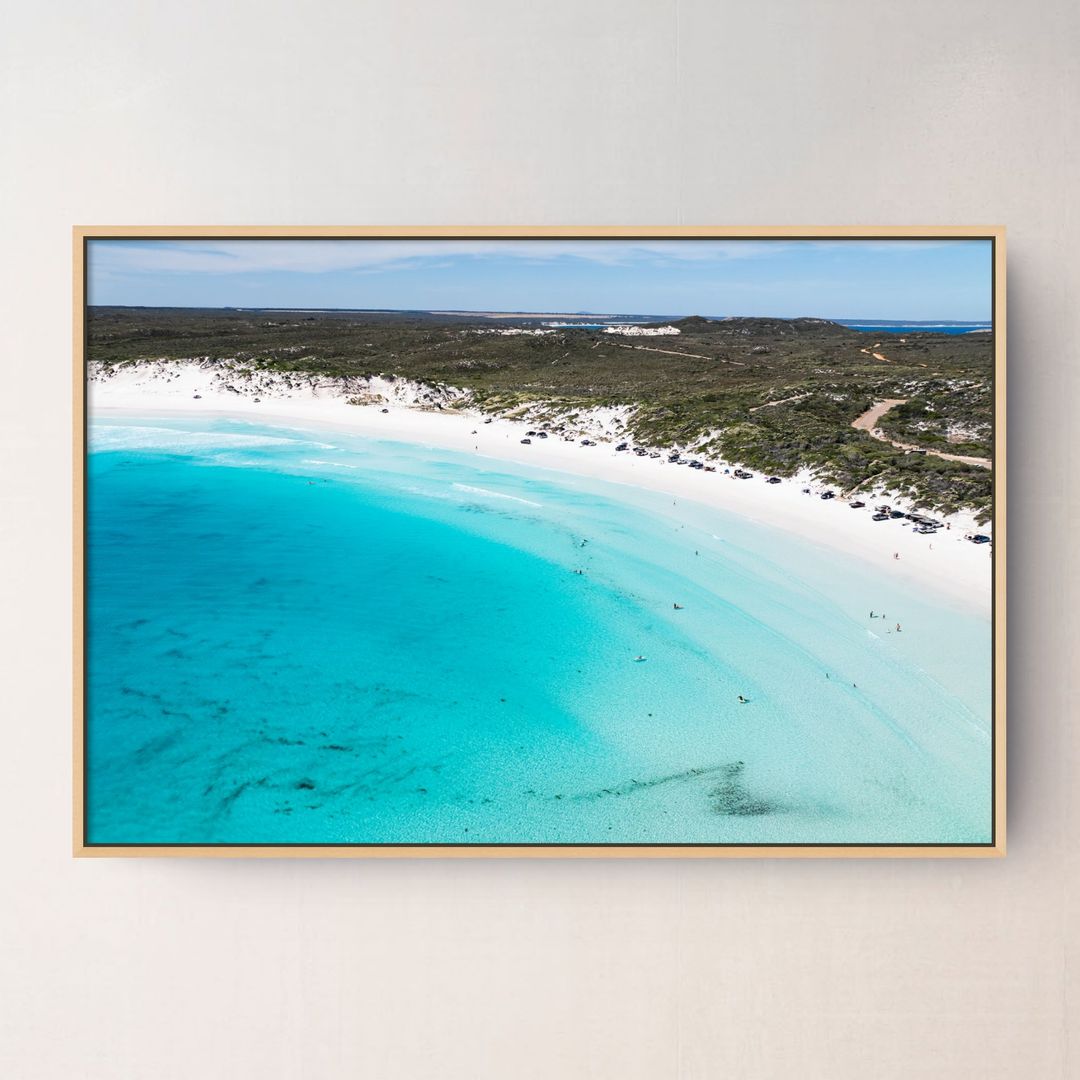 An oak framed aerial photograph of Wharton  Beach Esperance Australia with turquoise water, white sand, and green vegetation, displayed on a light beige wall.