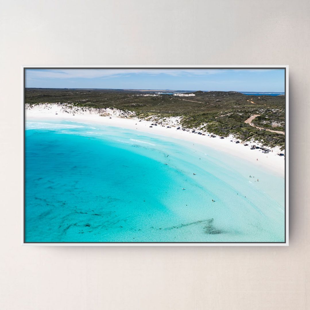 A white framed aerial photograph of Wharton  Beach Esperance Australia with turquoise water, white sand, and green vegetation, displayed on a light beige wall.